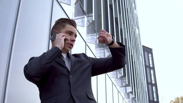 Takım elbiseli genç bir işadamı telefonda konuşuyor. Ciddi bir adam ayna iş merkezinin önünde duruyor. — Stok fotoğraf