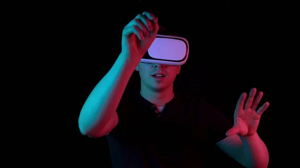 Fiatalember Vr szemüvegben. Egy ember, aki belemerül a virtuális valóságba, mozdulatokat tesz a kezével. Kék és piros fény esik egy ember a fekete háttér. — Stock Fotó