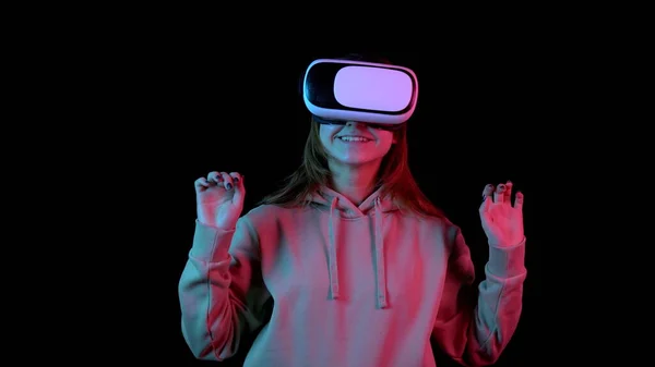 Молода жінка в окулярах VR. Жінка, занурена у віртуальну реальність, робить рухи руками. Блакитне і червоне світло падає на жінку на чорному тлі . — стокове фото