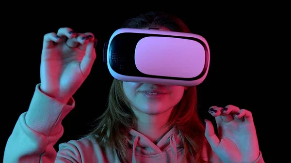 Fiatal nő Vr szemüvegben közelkép. Egy nő, aki belemerül a virtuális valóságba, mozdulatokat tesz a kezével. Kék és piros fény esik egy nő a fekete háttér. — Stock Fotó