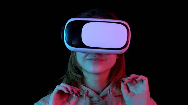 Jonge vrouw in Vr glazen close-up. Een vrouw ondergedompeld in virtual reality maakt bewegingen met haar handen. blauw en rood licht valt op een vrouw op een zwarte achtergrond. — Stockfoto