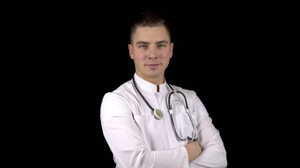 Ein junger Arzt dreht seinen Kopf in die Kamera und lächelt. ein Mann steht mit einem Stethoskop um den Hals auf schwarzem Hintergrund. — Stockfoto