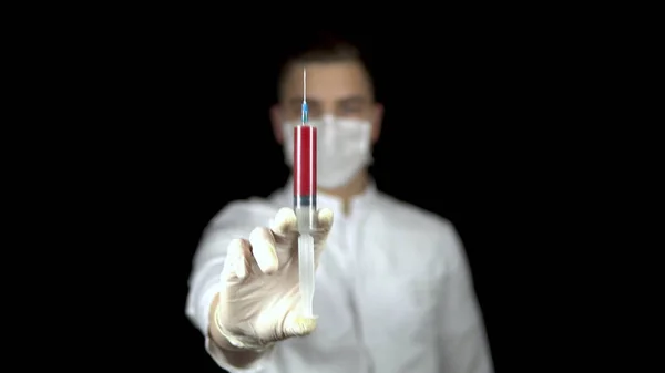 Sangue in una siringa primo piano su fondo nero. Un medico uomo porge una siringa con il sangue alla macchina fotografica . — Foto Stock