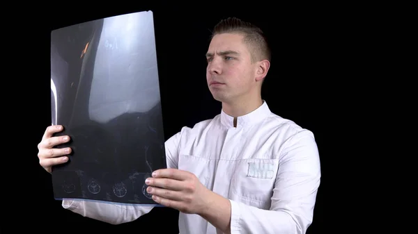 Een jonge man dokter controleert de resultaten van een MRI scan van een wervelkolom. Een man onderzoekt een MRI-beeld en toont dan een duim omhoog. Positief MRI resultaat. Op een zwarte achtergrond. — Stockfoto