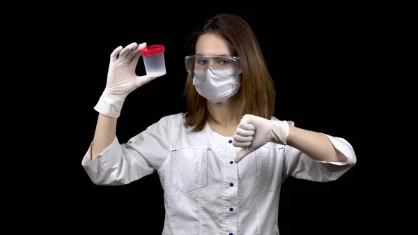 Jeune femme médecin vérifie les tests de sperme. La femme examine le bocal de test, puis montre un pouce vers le bas. Analyse négative du sperme. Sur fond noir . — Photo