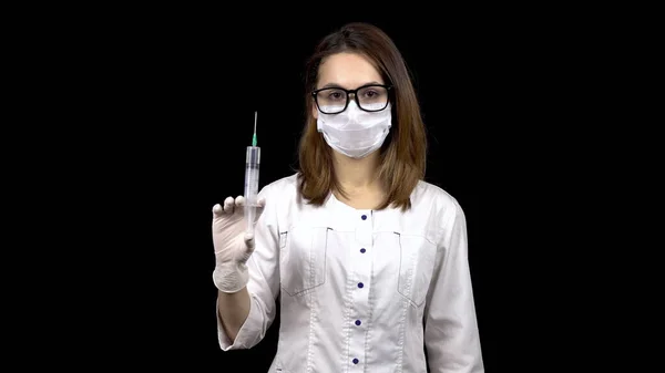 Young woman doctor is standing with a syringe filled with medication. A doctor sprays from a syringe to release air on a black background.