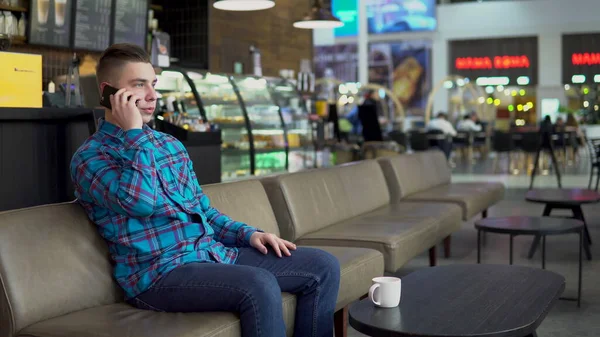 Молодий чоловік сидить у кафе з телефоном. Чоловік листується на смартфоні і п'є каву. Крупним планом . — стокове фото