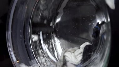 Çamaşır makinesi çalışıyor. Çamaşır makinesi, içi kıyafet dolu bir varili döndürür. Davul yakın çekim.
