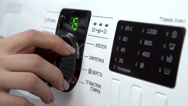 A young woman turns on a washing machine. A woman turns the lever choosing the mode on the washing machine. Hand close-up. — Stock Photo, Image