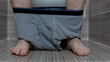 Adam tuvalette otururken gri külotunu çıkardı. Tuvalette kıllı bacaklı bir adam.