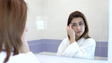 Genç bir kadın makyajını pamukla temizliyor. Banyodaki aynanın önünde beyaz bornozlu bir kız. Aynaya bak.