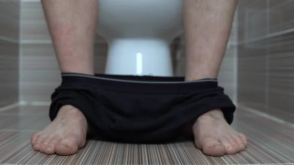 Muž si sundal černé kalhotky, když seděl na záchodě. Muž s chlupatýma nohama na záchodě — Stock fotografie