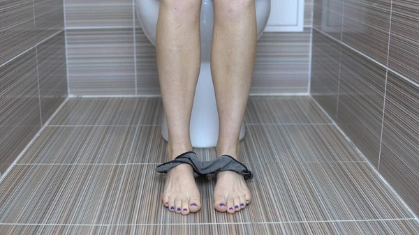 Femme a tiré gris tanga culotte assise sur les toilettes. Fille avec les jambes rasées sur les toilettes — Photo