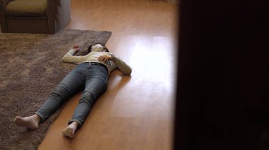 Genç bir kadın yerde ölü yatıyor. Tıbbi maskeli bir kadın yerde baygın yatıyor. Kapının manzarası..