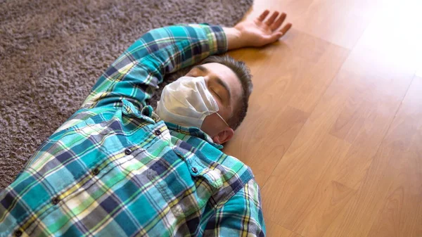 En ung man ligger död på golvet. En man i medicinsk mask ligger på golvet i medvetslöshet. Utsikt ovanifrån. — Stockfoto