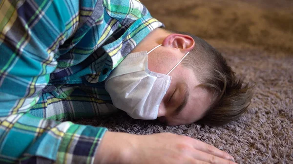 Um jovem cai no chão. Um homem com uma máscara médica jaz no chão da inconsciência . — Fotografia de Stock