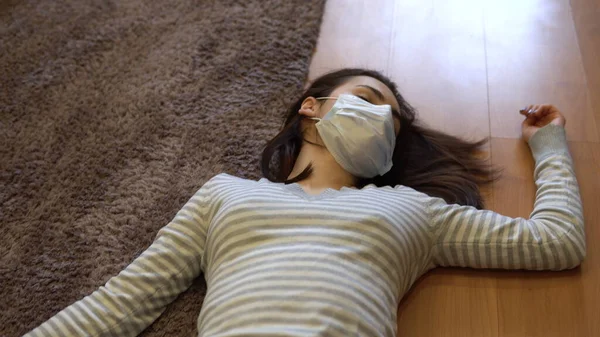 O tânără zace pe podea moartă. O femeie cu o mască medicală se află pe podeaua inconştienţei. Vedere de sus . — Fotografie, imagine de stoc