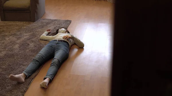 Uma jovem deita-se no chão morta. Uma mulher com uma máscara médica está inconsciente no chão. A vista da porta . — Fotografia de Stock