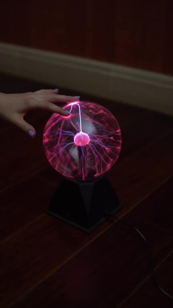 La main féminine touche la boule de plasma, distribuant de petits éclairs. Expériences avec l'électricité dans le noir. Vidéo verticale. Vidéo verticale .
