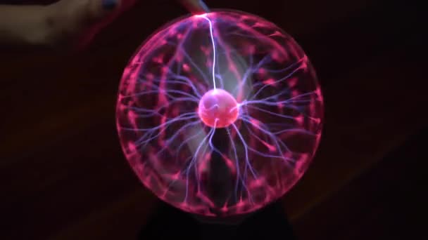 Une main féminine touche une boule de plasma qui émet de petits éclairs. Expériences avec l'électricité dans l'obscurité . — Video