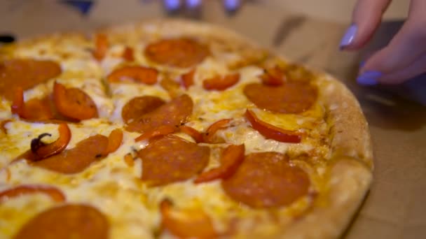 Uma jovem pega uma fatia de pizza com um queijo espalhado. Uma pizza inteira está sobre a mesa. Mão segurando uma grande plone . — Vídeo de Stock