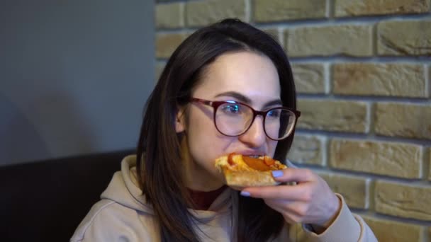 Una joven está comiendo una rebanada de pizza. Mujer sentada en un restaurante y comiendo pizza de cerca . — Vídeos de Stock