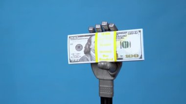 Mekanik bir el bir paket dolar tutar. Gri sayborg bir el mavi bir arkaplanda para tutuyor..