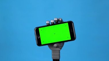 Mekanik bir el yeşil ekranlı bir telefonu tutar. Mavi arka planda akıllı telefon tutan gri sayborg el. Krom anahtar.