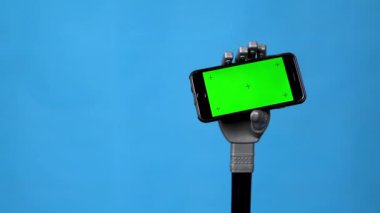 Mekanik bir el yeşil ekranlı bir telefonu tutar. Mavi arka planda akıllı telefon tutan gri sayborg el. Krom anahtar.