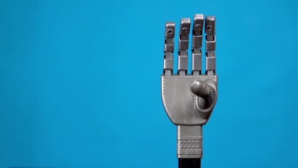 Una mano mecánica flexiona los dedos y muestra una señal de roca. Brazo cyborg gris cobró vida y comenzó a moverse sobre un fondo azul . — Vídeo de stock