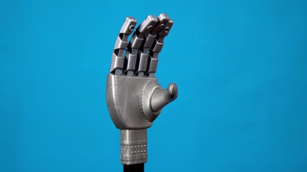 Une main mécanique fléchit ses doigts et montre un signe de roche. Gris cyborg bras est venu à la vie et a commencé à se déplacer sur un fond bleu . — Video