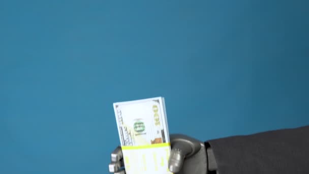 Cyborg affärsman i kostym har ett paket dollar. En mekanisk hand visar en bunt pengar på en blå bakgrund. — Stockvideo
