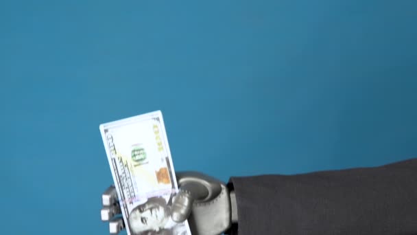 Un hombre de negocios cyborg con traje tiene un paquete de dólares. Una mano mecánica muestra un paquete de dinero sobre un fondo azul . — Vídeo de stock