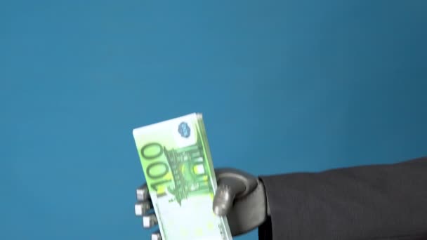 Cyborg hombre de negocios en un traje tiene un paquete de euros. Una mano mecánica muestra un paquete de dinero sobre un fondo azul . — Vídeos de Stock