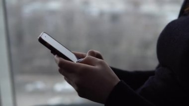 Telefonu yakın çekim yapan genç bir kadın. Panoramik pencerenin yanındaki kafede elinde akıllı bir telefonla oturan bir kız. Pencereden görüntüle.