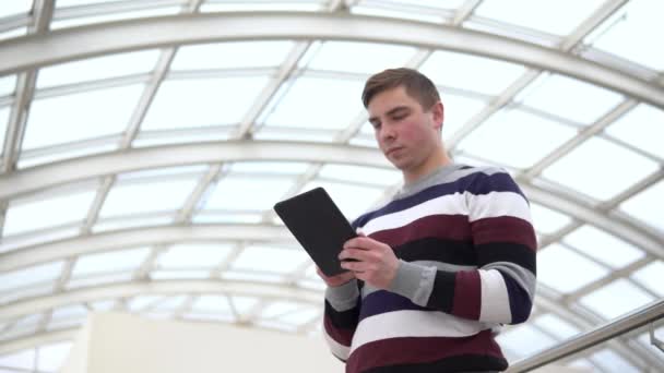 Un joven está de pie con una tablilla. Un hombre usa una tableta contra un techo de cristal. Una persona ocupada está enviando mensajes en el mensajero . — Vídeos de Stock