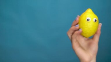 Bir kadının elinde gözleri olan bir limon. Lemon çerçevenin içine atlıyor ve mavi bir arka planda etrafına bakıyor. Kadın eli yakın çekim.
