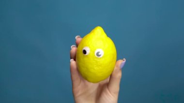 Lemon 'un gözleri bir kadının elinde, yakın plan. Limon mavi bir arka planda gözleri titretir ve döndürür. Yavaş çekim.
