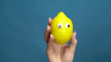Lemon 'un gözleri bir kadının elinde, yakın plan. Limon mavi bir arka planda gözleri titretir ve döndürür. Yavaş çekim.