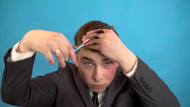 Businessman cutting his own hair on a blue background. A man in a suit trimmed himself with scissors. — Stock Video