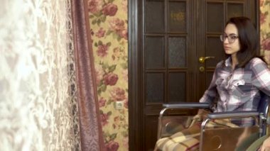 Tekerlekli sandalyedeki genç bir kadın pencereden dışarı bakıyor. Kız tekerlekli sandalyeyle evdeki pencereye doğru gidiyor..