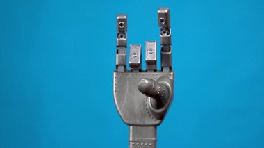 Mekanik bir el parmaklarını esnetir ve bir kaya işareti gösterir. Mavi arka planda gri cyborg kolu.