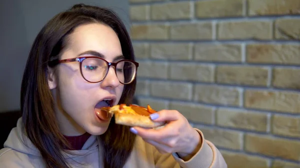 Una ragazza sta mangiando una fetta di pizza. Donna seduta in un ristorante e mangiare pizza primo piano . — Foto Stock