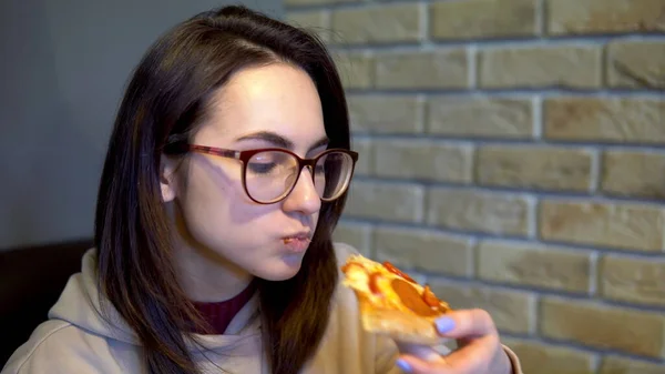 Uma jovem está comendo uma fatia de pizza. Mulher sentada em um restaurante e comendo pizza close-up . — Fotografia de Stock