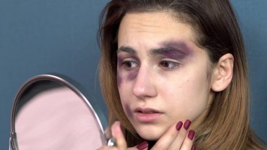 Genç bir kadın aynada yüzündeki morlukları inceliyor. Genç bir ailede kavgalar. Aile içi şiddet. Kapat.