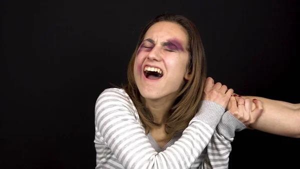 El hombre agarró a la joven por el pelo. Una mujer con moretones en la cara. Peleas en una familia joven. Violencia doméstica. Sobre un fondo negro — Foto de Stock