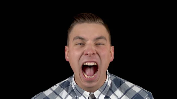 The young man is screaming. A man screams strongly in a shirt on a black background closeup — Stock Photo, Image