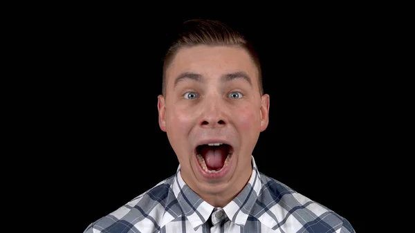 The young man shows emotions of surprise on his face. Surprised man in a shirt on a black background closeup — Stock Photo, Image