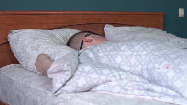Mladý muž nemůže usnout ve spánkové masce. Muž leží v posteli ve svém pokoji a trpí nespavostí. — Stock video