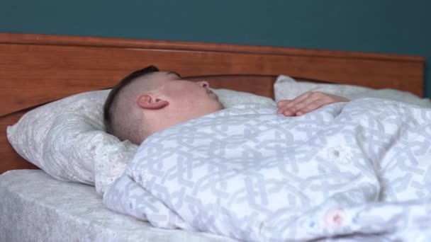 Un joven está durmiendo bajo las sábanas. Un hombre yace en la cama en su habitación . — Vídeos de Stock
